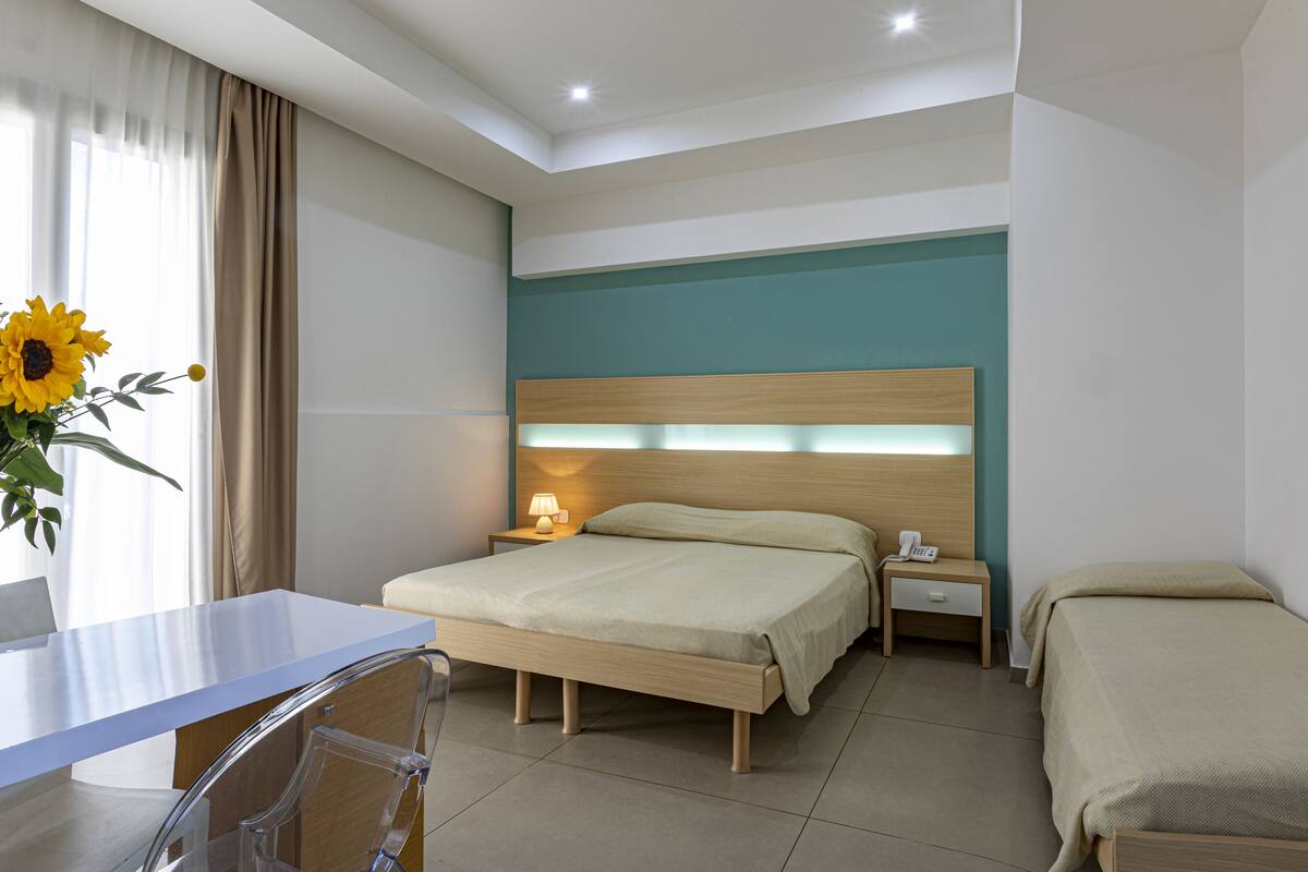 A hotel room with a bed, bedside table, lamp, and a desk with a chair.