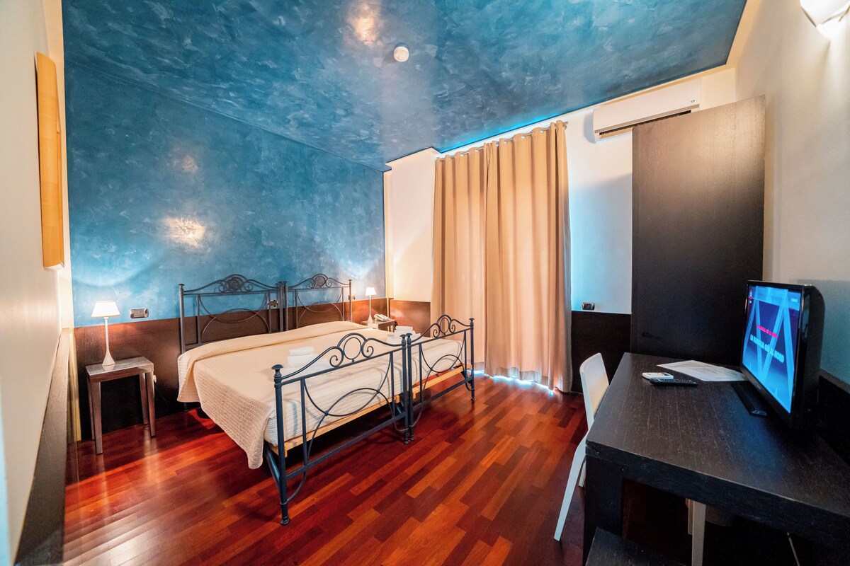 A bedroom with a bed, bedside tables, a desk, a chair, a TV, and a window with curtains.