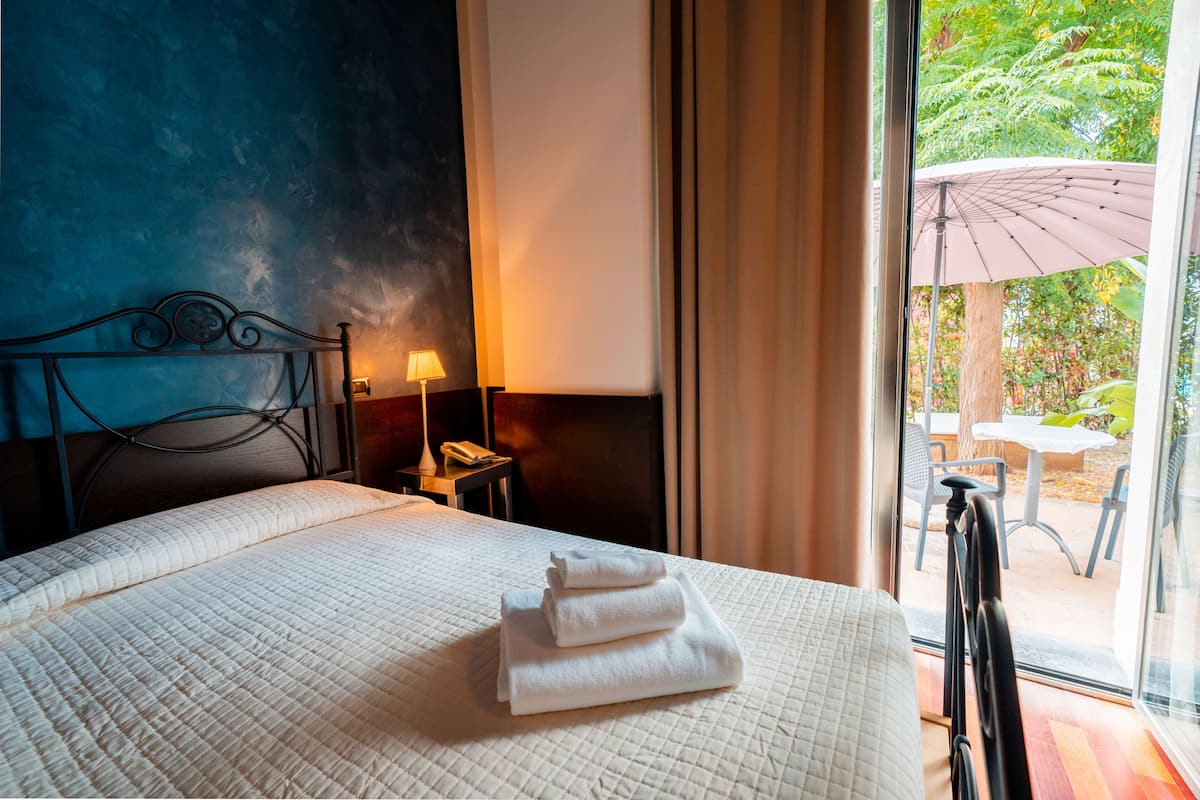 A hotel room with a bed, a nightstand, a lamp, and a view of an outdoor patio.