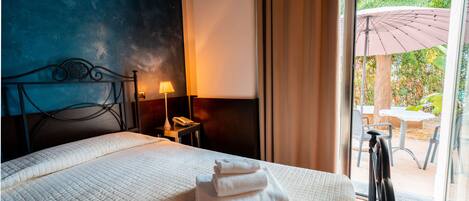 A hotel room with a bed, a nightstand, a lamp, and a view of an outdoor patio.
