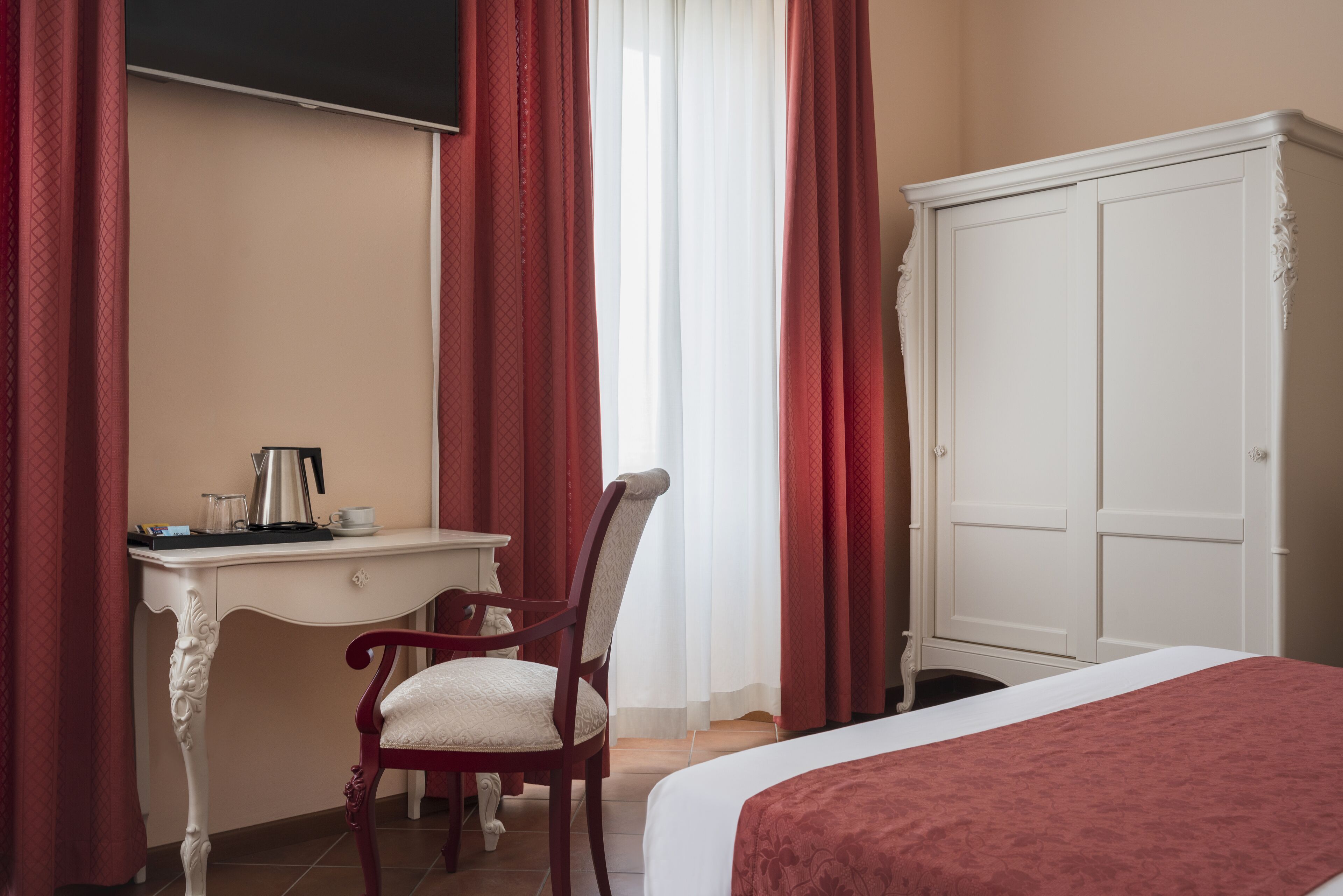 A hotel room with a bed, a desk with a coffee maker, a chair, and a wardrobe.