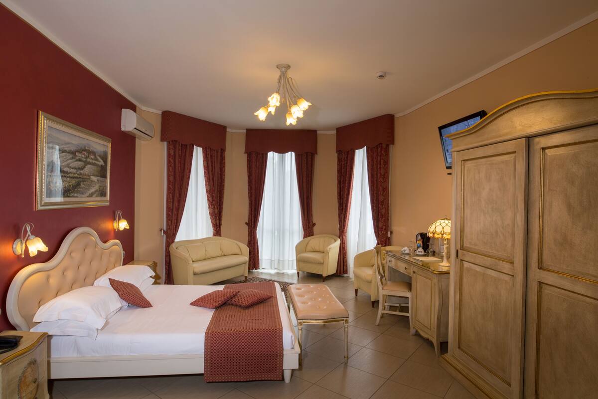 Ein Hotelzimmer mit einem großen Bett, zwei Sesseln, einem Schreibtisch und einem Kleiderschrank.