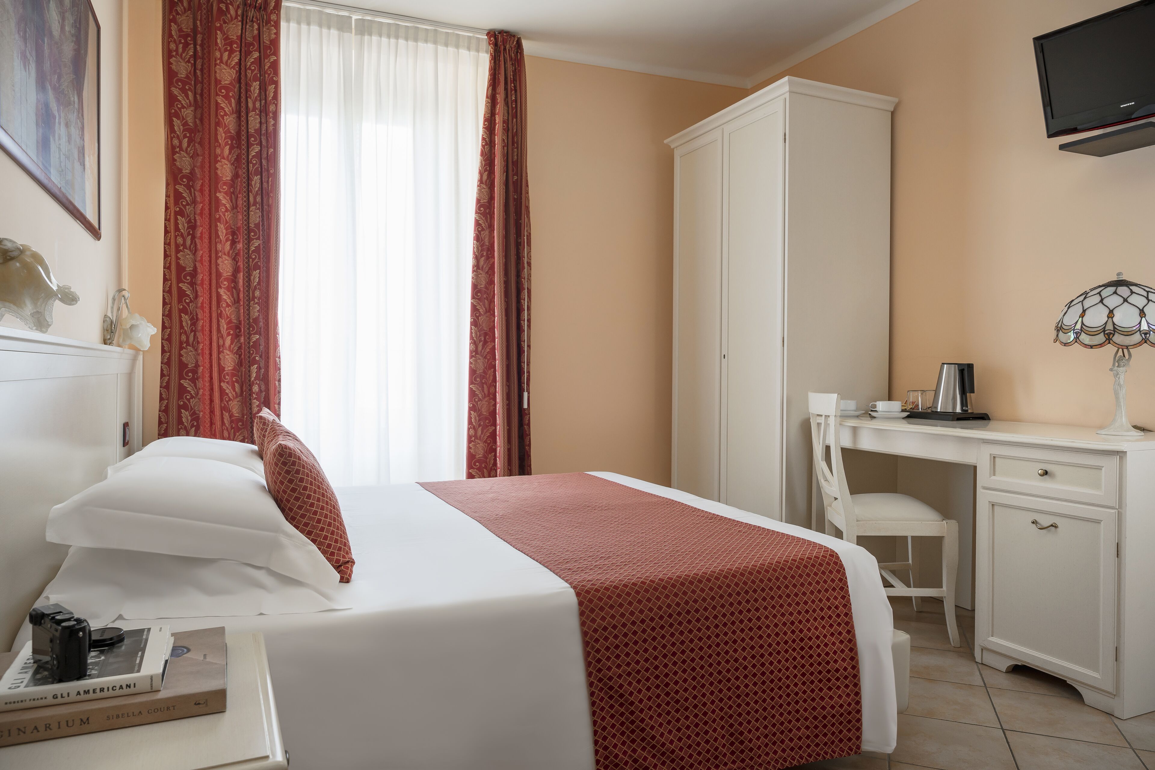Una habitación de hotel con cama, escritorio, silla, armario y televisor.
