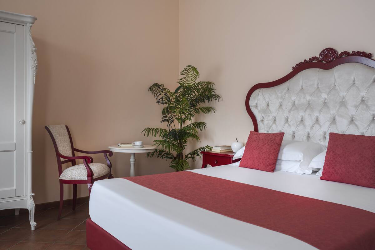 Ein Hotelzimmer mit einem großen Bett, einem Sessel, einem kleinen Tisch und einer Topfpflanze.