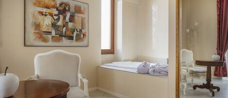 A modern bathroom with a bathtub, a white chair, a round wooden table, and a large mirror.
