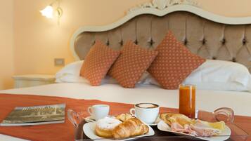 Ein Frühstücksbrett mit Croissants, Schinken und Eiern auf einem Bett mit einem gebogenen, gesteppten Kopfteil und gemusterten Kissen.