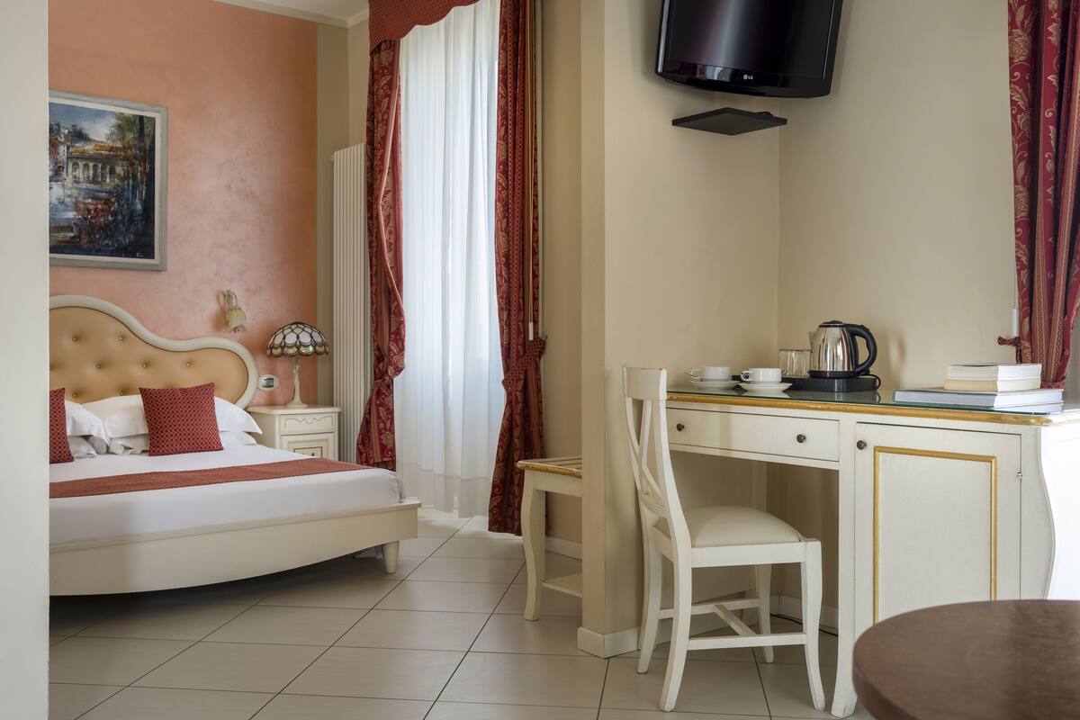Ein Hotelzimmer mit einem Bett, einem Schreibtisch, einem Sessel, einem Fernseher und einem Bild an der Wand.