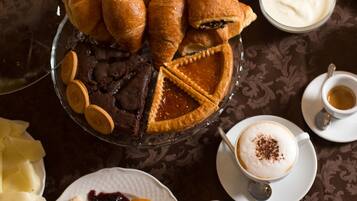 Una selezione di prodotti da forno, tra cui pane, pasticcini e una torta, accompagnati da frutta e una tazza di caffè.