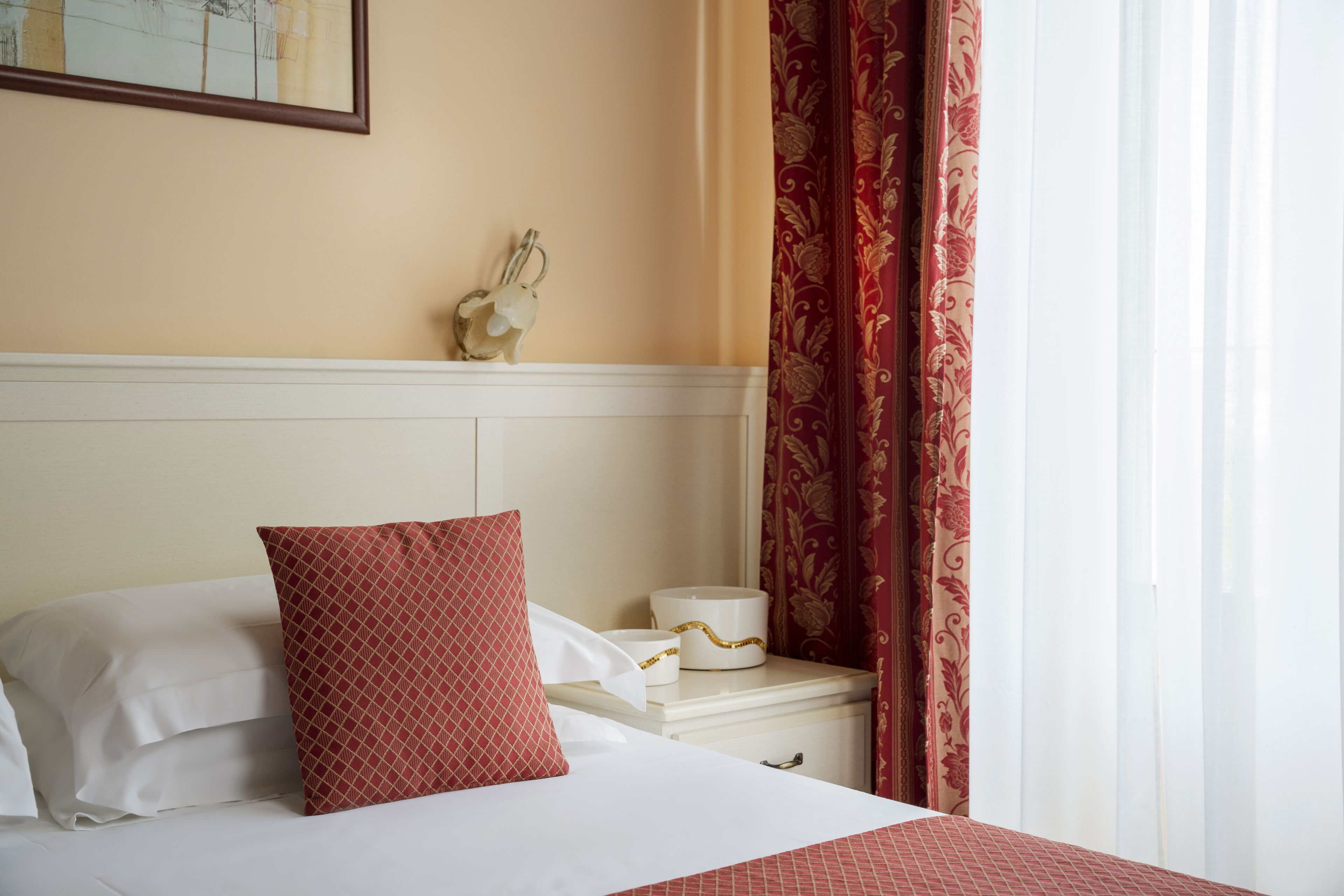 A hotel room with a neatly made bed, a nightstand with a decorative item, and a window with curtains.