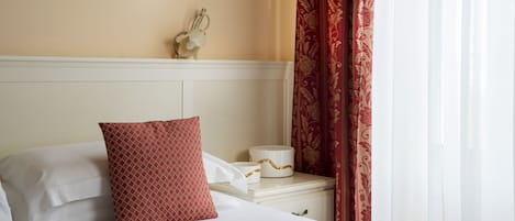 A hotel room with a neatly made bed, a nightstand with a decorative item, and a window with curtains.