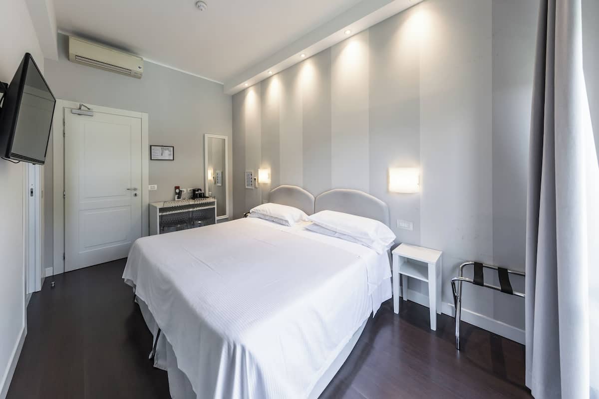 Ein Hotelzimmer mit einem großen Bett, Nachttischen, einem Fernseher, einem Spiegel und einer wandmontierten Lampe.