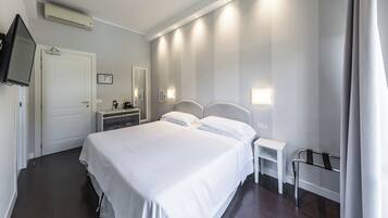 Habitación de hotel con una cama grande, mesitas de noche, un televisor, un espejo y una lámpara fijada a la pared.