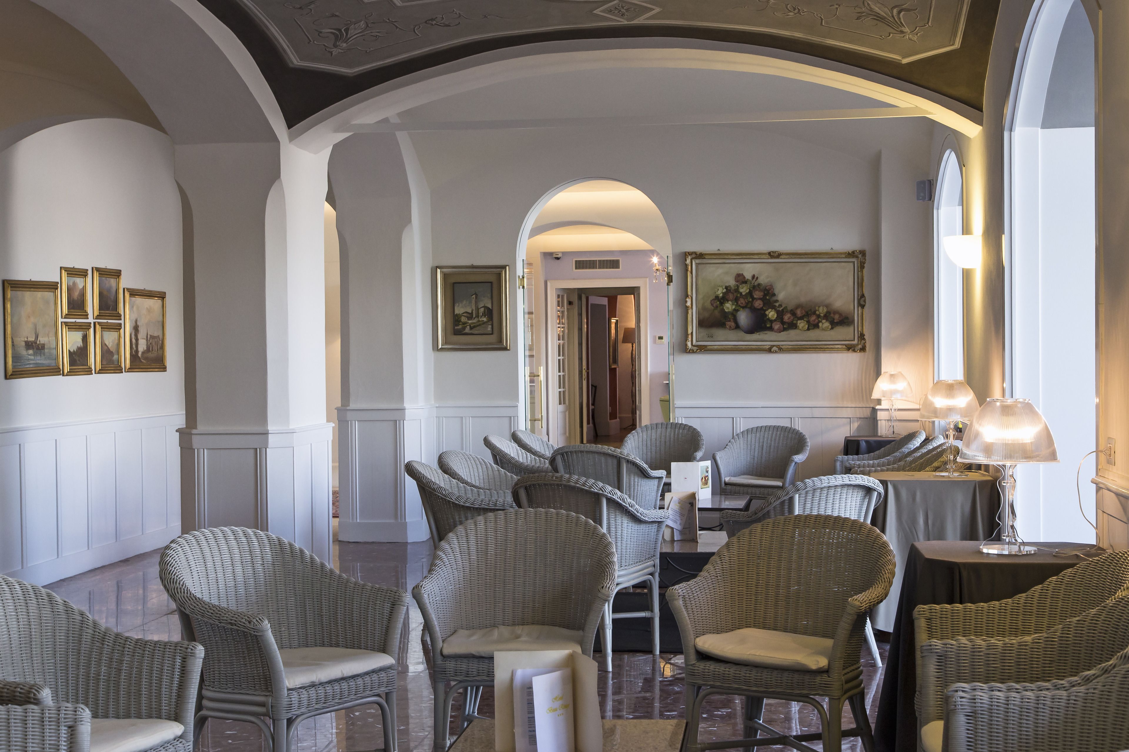A hotel lobby with wicker chairs, framed artwork, and a chandelier.