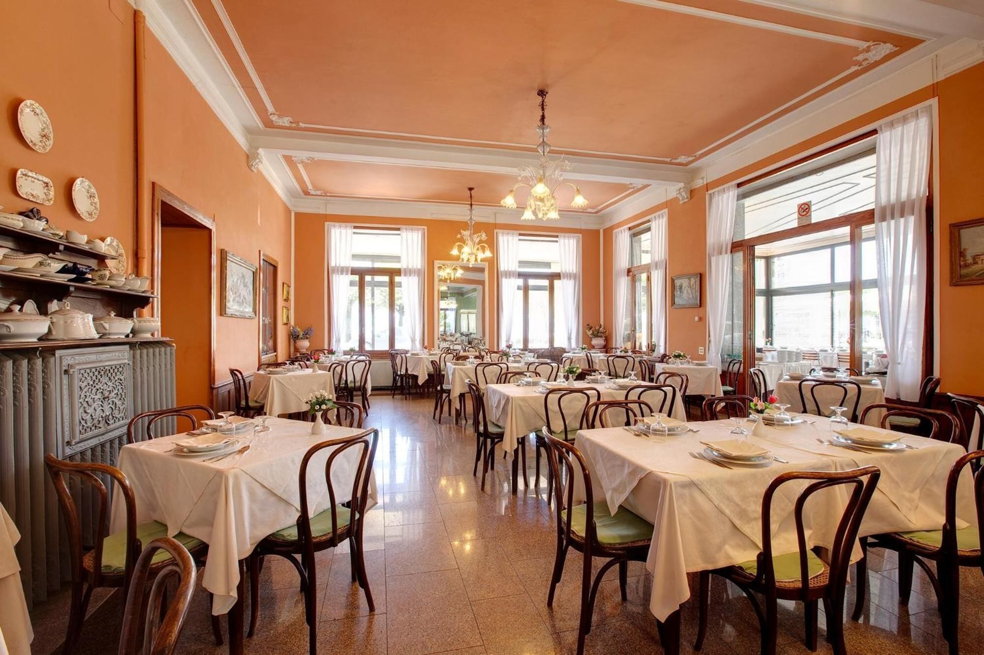 A dining area with multiple tables and chairs, large windows, and decorative lighting.