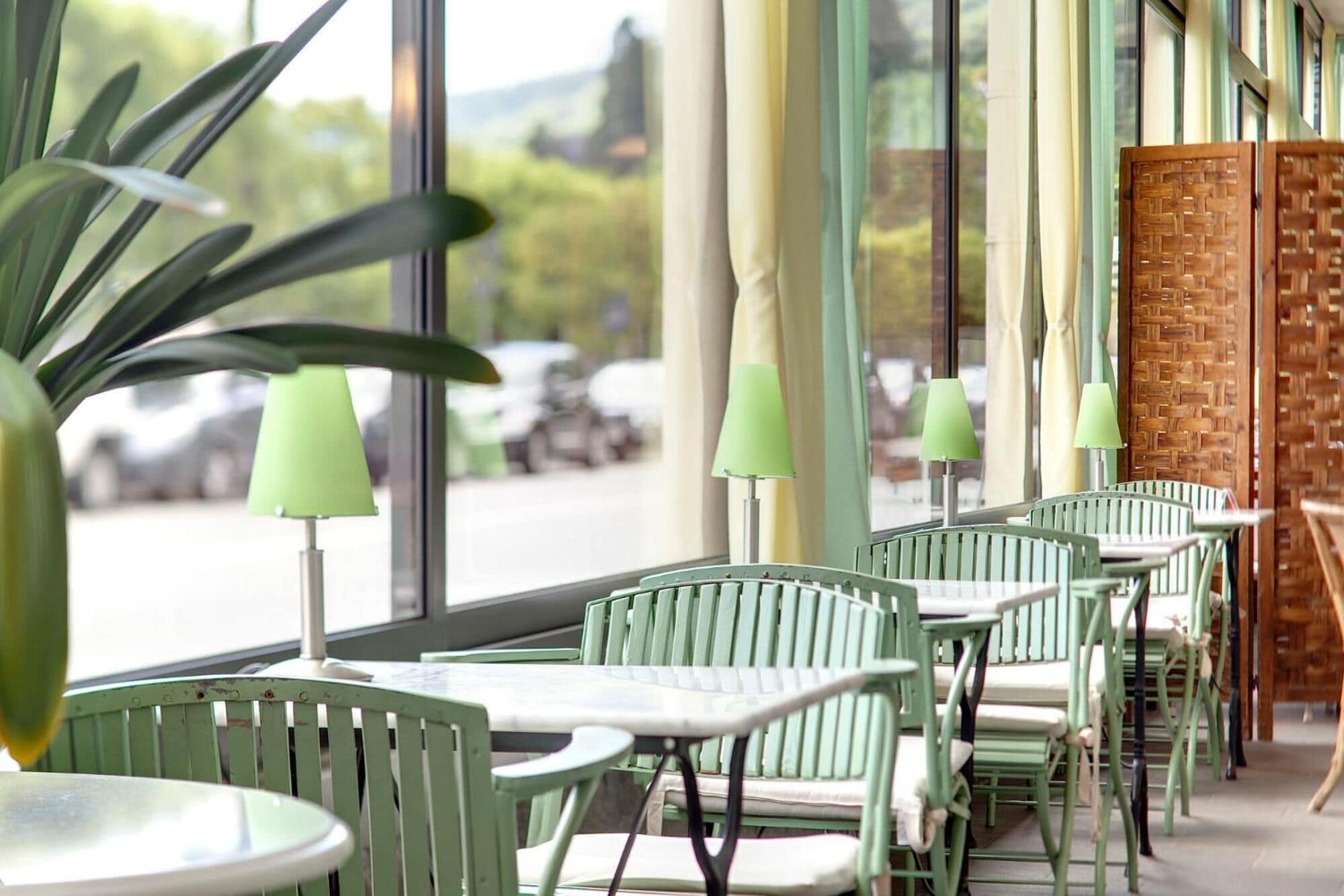 Filas de sillas y mesas verdes dentro de una cafetería con ventanas amplias.