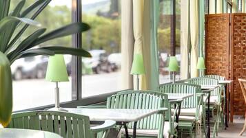 Filas de sillas y mesas verdes dentro de una cafetería con ventanas amplias.
