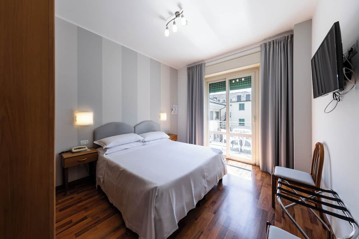 Ein Hotelzimmer mit Bett, Nachttisch, Sessel, Fernseher und Blick nach draußen.