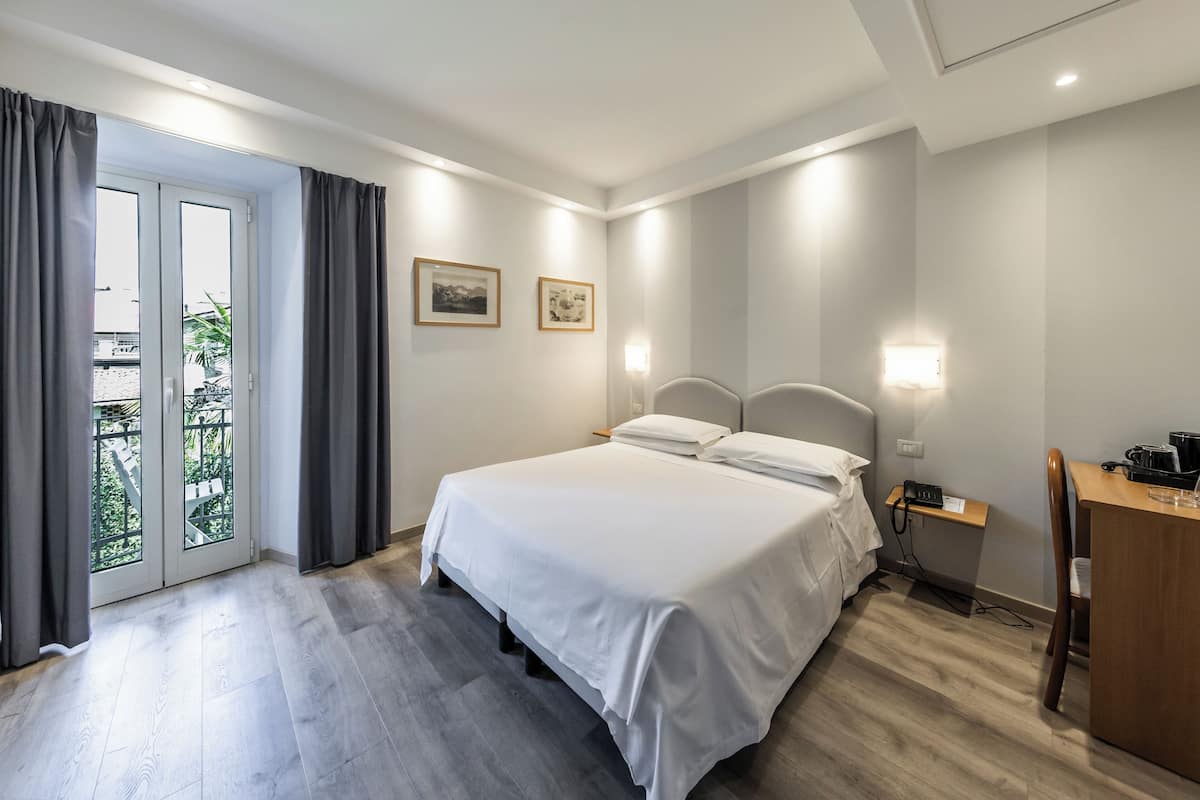 Ein Hotelzimmer mit Bett, Schreibtisch, Stuhl, Nachttisch und einer Schiebetür zum Balkon.