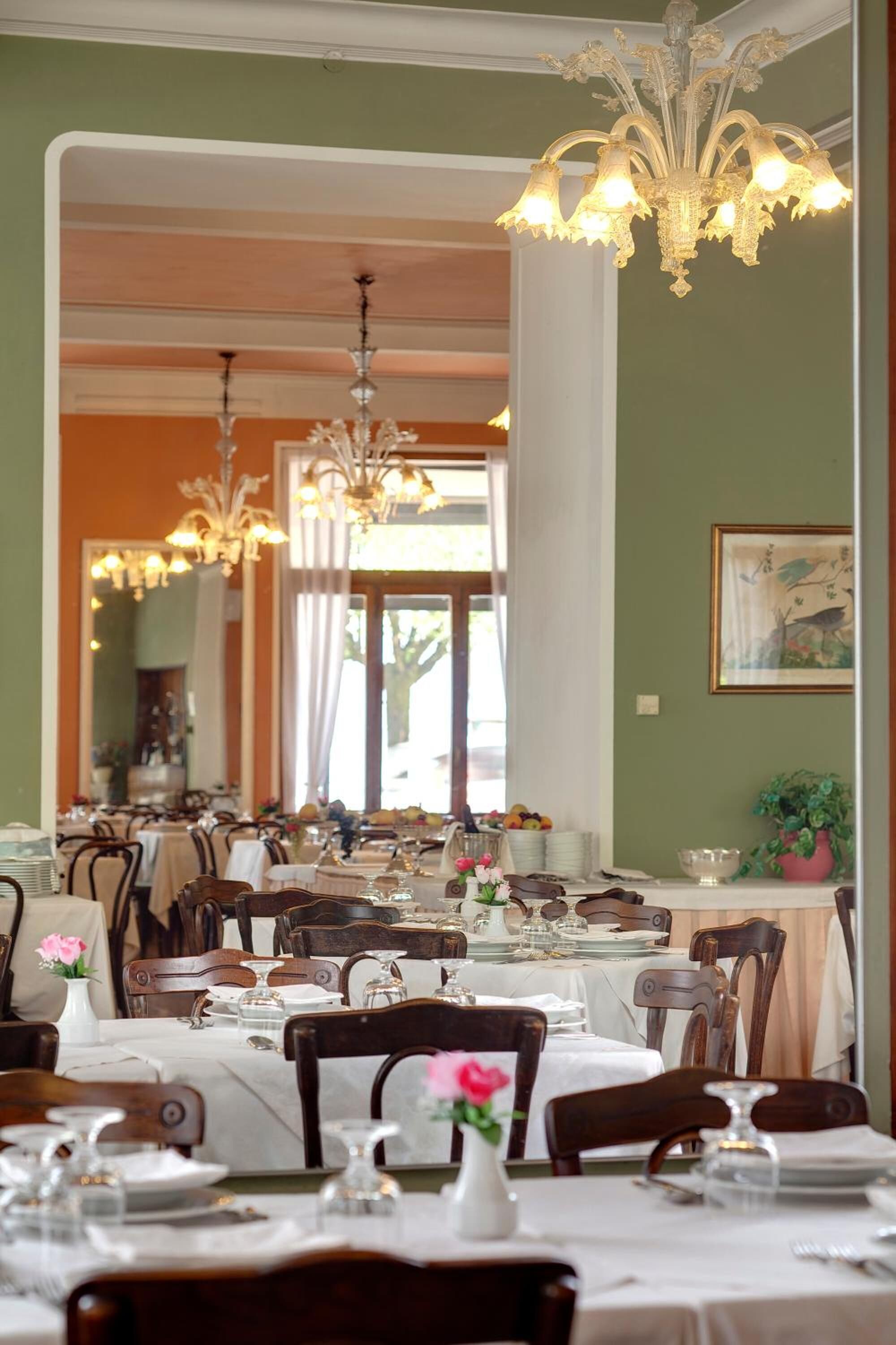 A dining area with multiple tables set for service, elegant chandeliers, and a large mirror reflecting the room.