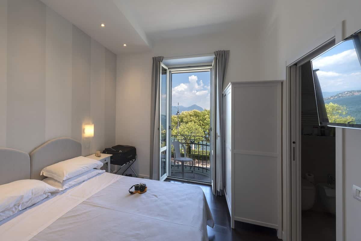 Ein Hotelzimmer mit Bett, Schreibtisch, Stuhl und einem Balkon mit Blick auf das Meer und die Berge.