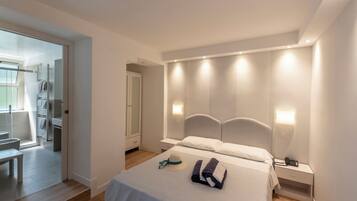 Un dormitorio moderno con cama, mesitas de noche y un banco en la esquina. Se ve una puerta que da a un baño.