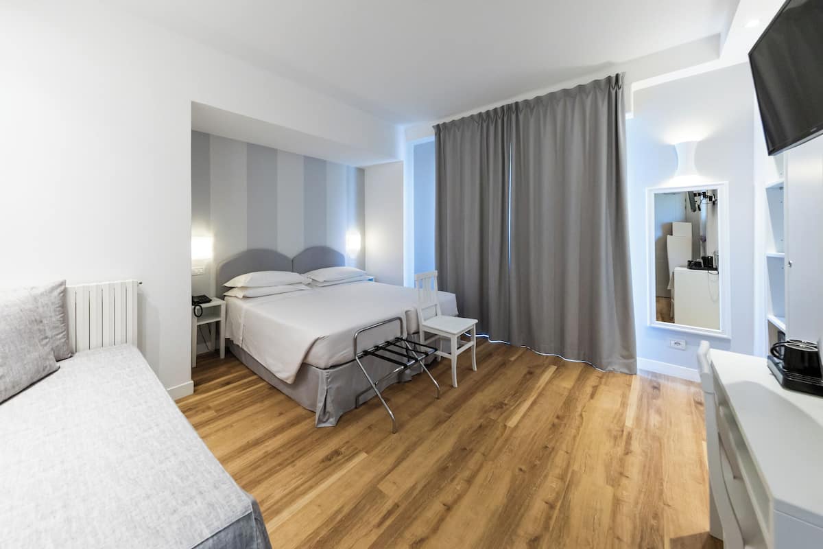 Ein modernes Hotelzimmer mit Bett, Nachttisch, Sessel und kleinem Schreibtisch mit Lampe.