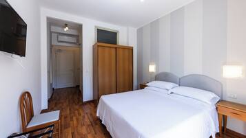 Un dormitorio con cama, mesita de noche, silla, armario y televisor montado en la pared.