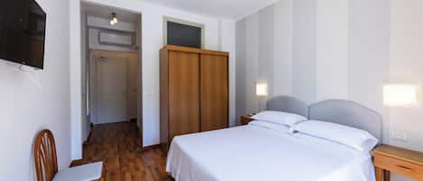 A bedroom with a bed, bedside table, chair, wardrobe, and a TV mounted on the wall.