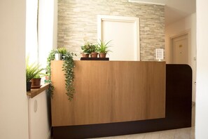 Un mostrador de recepción con detalles de madera, plantas en macetas y una pared con diseño de piedra.