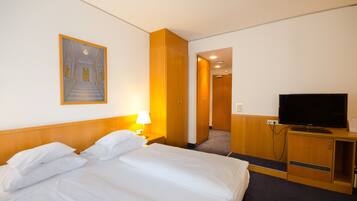 Habitación de hotel con cama, televisión, un cuadro y un pasillo que conduce a otra habitación.
