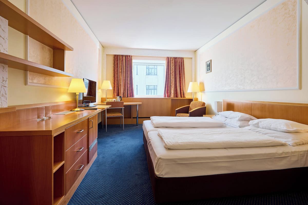 A hotel room with a bed, a desk, a chair, a TV, and a window with curtains.