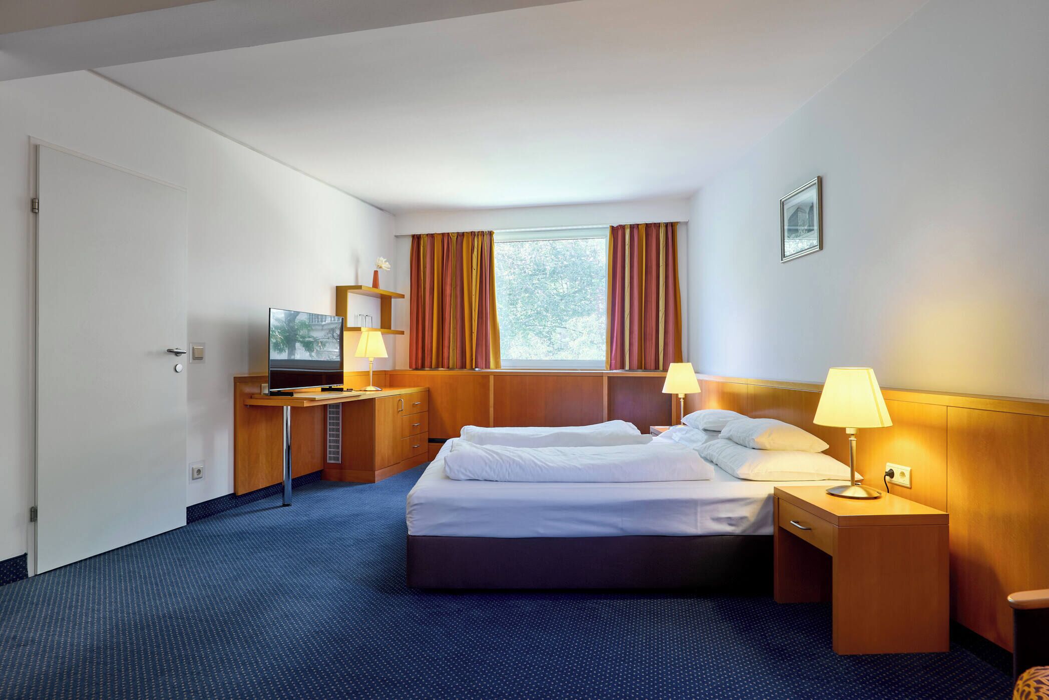 Ein Hotelzimmer mit Bett, Nachttischen, einem Schreibtisch, einem Fernseher und einem Fenster mit Vorhängen.