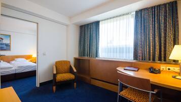 Una habitación de hotel con cama, escritorio, silla, ventana con cortinas y un cuadro en la pared.