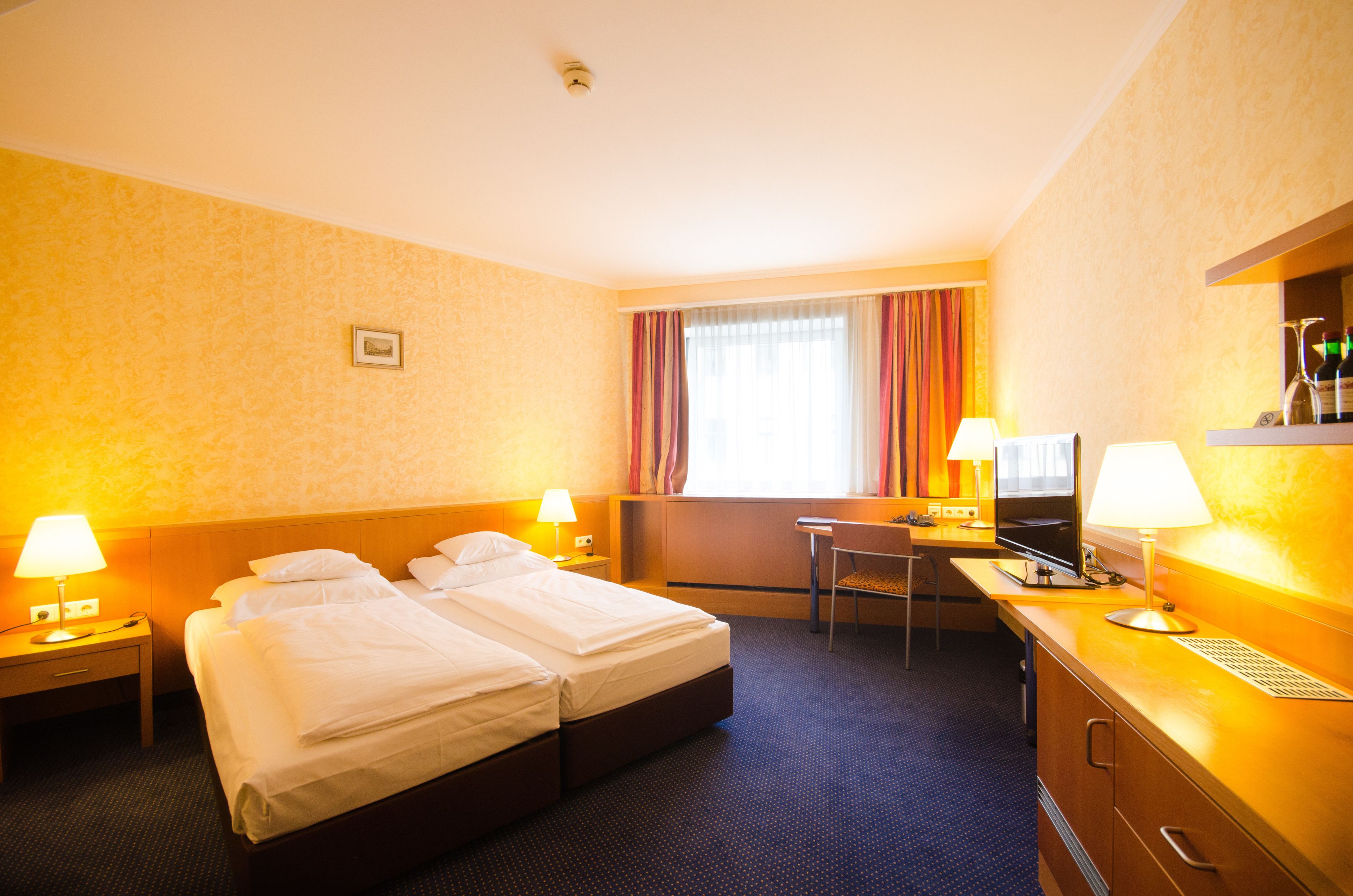 A hotel room with two beds, a desk with a computer, a TV, and a minibar.
