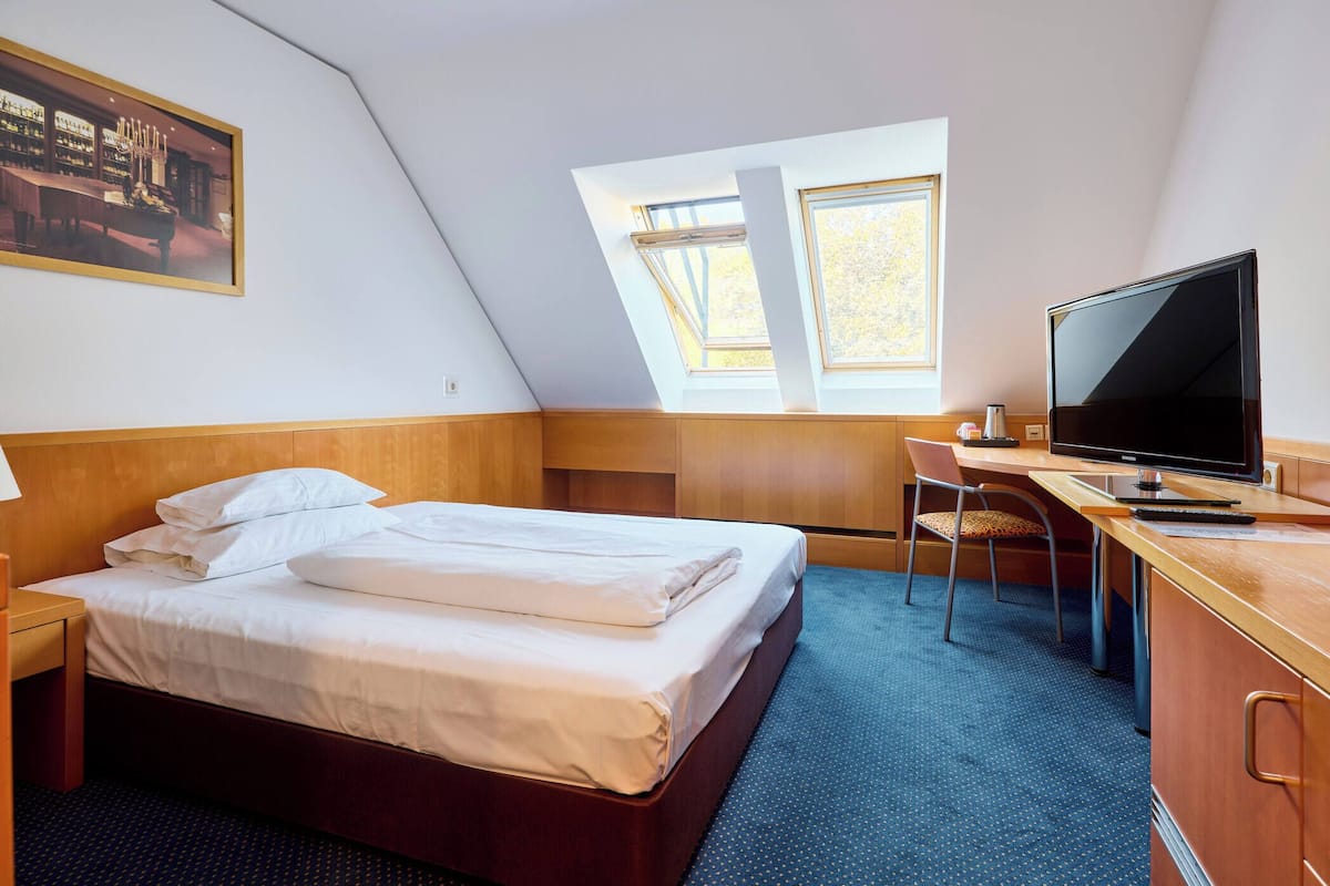 A hotel room with a bed, desk, television, and a painting on the wall.