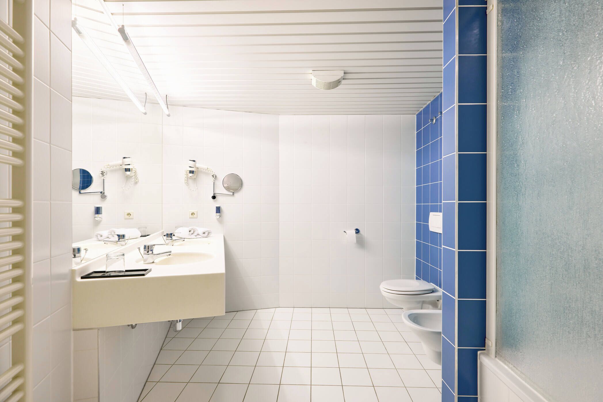 Une salle de bain avec un lavabo blanc, un miroir et des toilettes, et des murs recouverts de carreaux bleus.