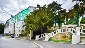 A hotel with a modern exterior, a stone staircase, and a large tree in front. - Hotel Strudlhof (Vienna)