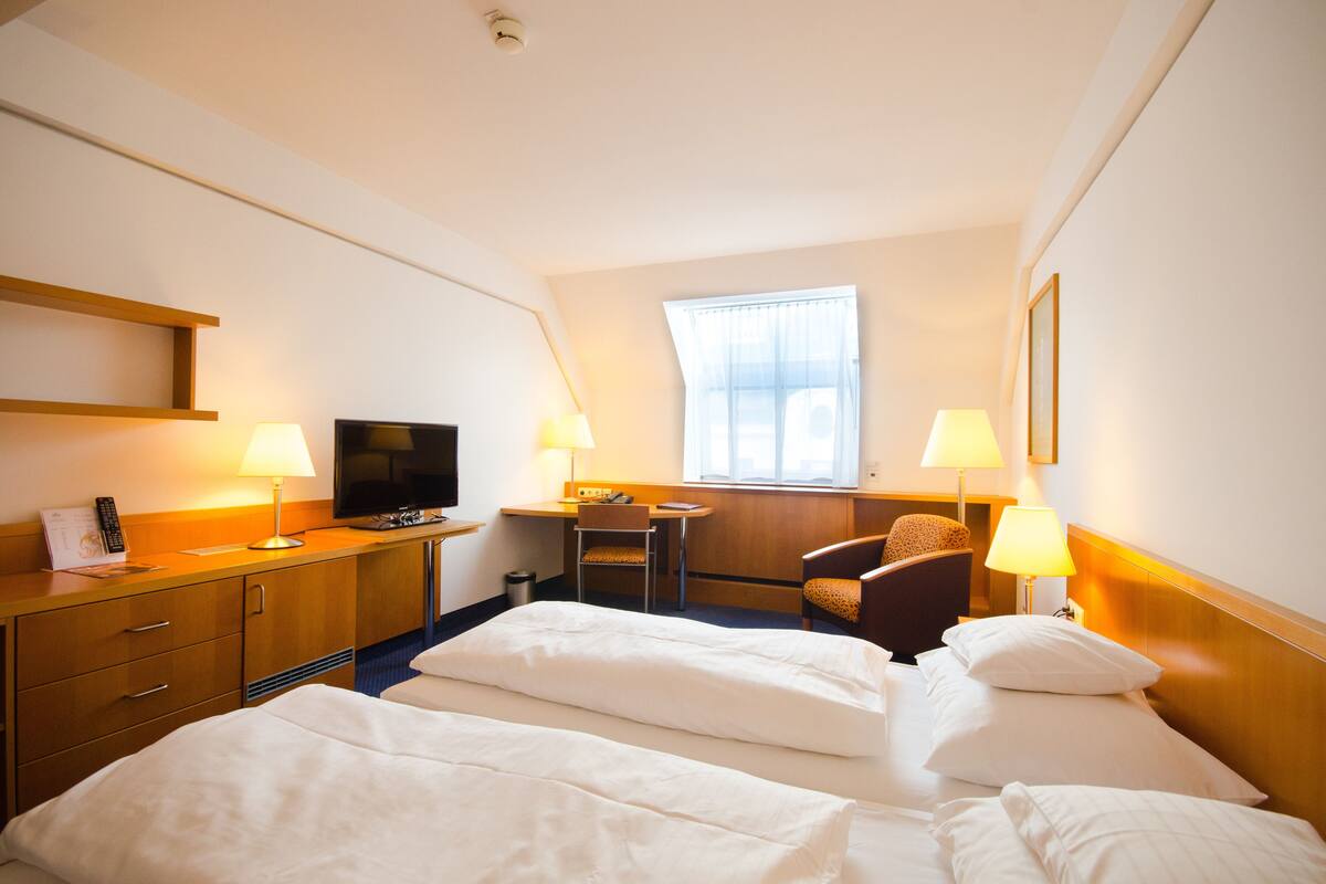 A hotel room with two beds, a desk, a television, and two lamps.