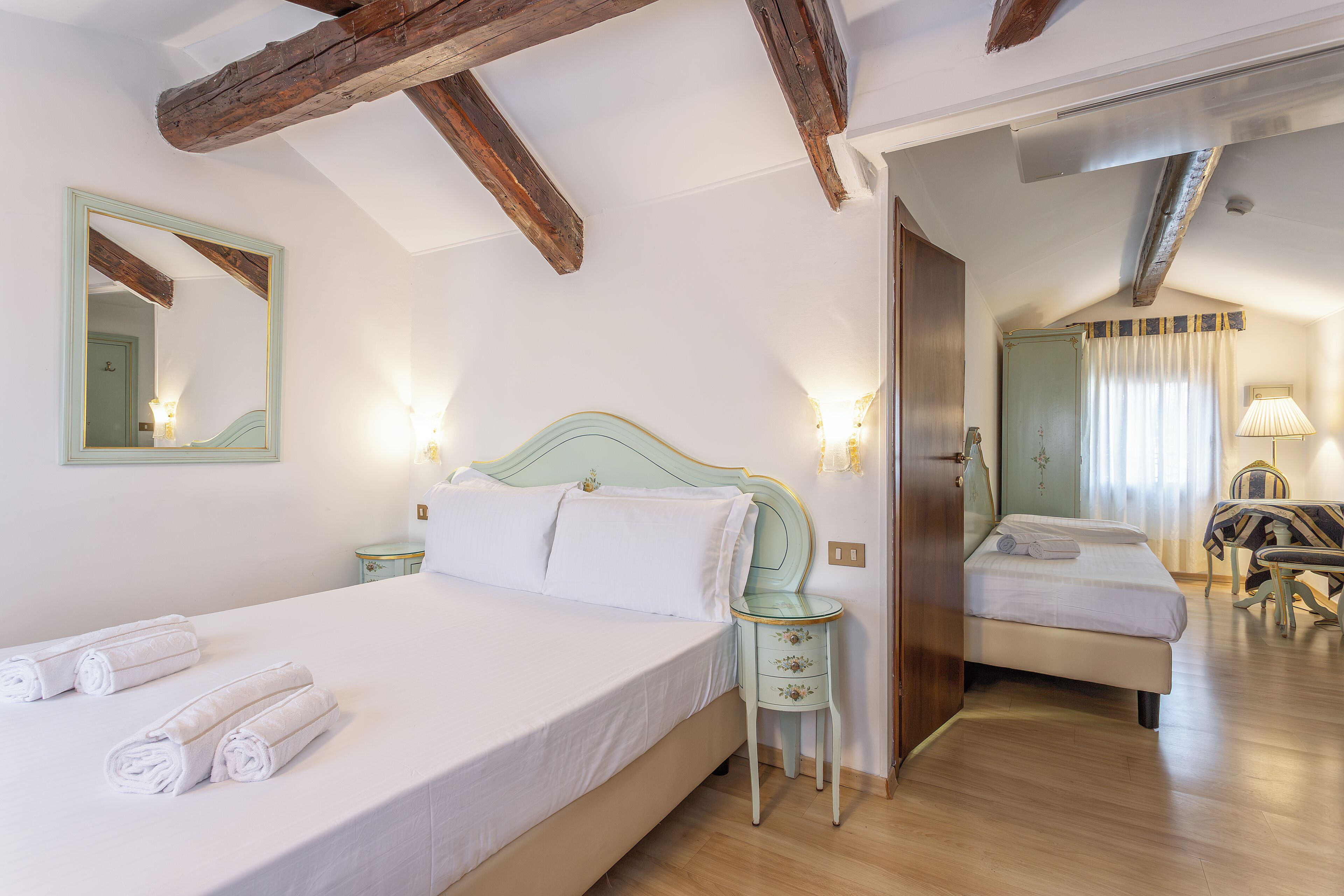 A hotel room with a bed, a bedside table, a mirror, and a door leading to another room.
