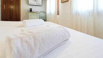 A neatly made bed with a rolled white towel, a framed sign reading 'HOTEL ORION' on the wall, and a wooden door.