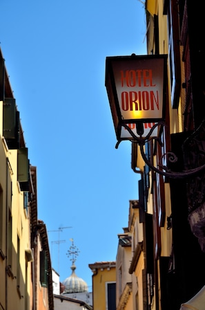 A hotel sign labeled "HOTEL ORION" in a narrow street with buildings on either side and a dome in the background. - Hotel Orion (Venice)