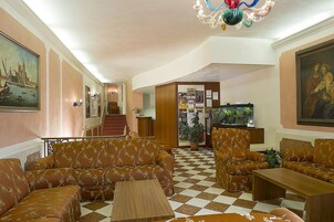 Un hall de hotel con sofás estampados, suelo a cuadros, una escalera y una araña.