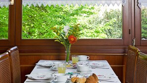 A dining area with a table set for breakfast, a window with a view of greenery, and a decorative letter "N" on the window. - Hotel Nazionale (Venice)