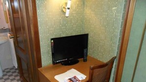 A small room with a wooden desk, a black TV, and a wicker chair. - Hotel Nazionale (Venice)