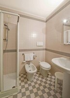 A bathroom with a shower, toilet, bidet, and sink.