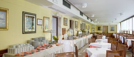Un comedor con mesas largas, sillas e imágenes enmarcadas en las paredes.