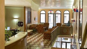 A lobby with a checkered floor, a reception desk, and a seating area with patterned furniture. - Hotel Nazionale (Venice)