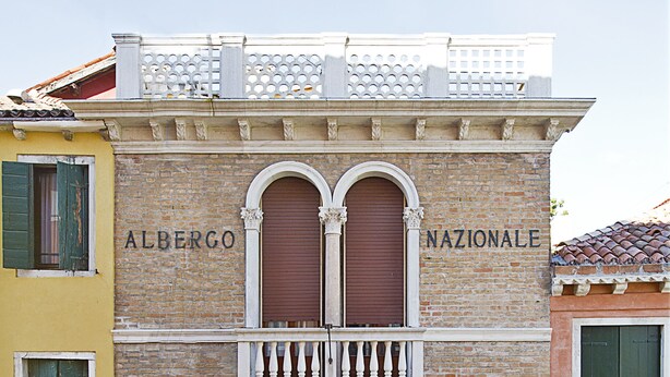 A building with the name "Alberghetto Nazionale" on the facade, featuring a balcony with balustrades, multiple windows with shutters, and a ground-level entrance. - Hotel Nazionale (Venice)