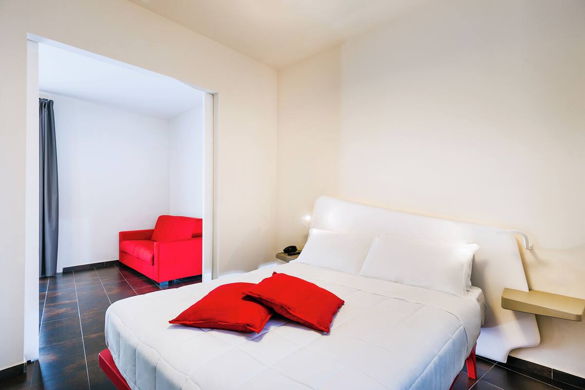 A hotel room with a bed, a red chair, and a nightstand with a phone.