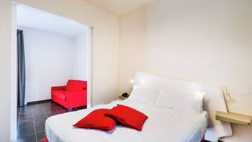 Una habitación de hotel con una cama, una silla roja y una mesita de noche con un teléfono.